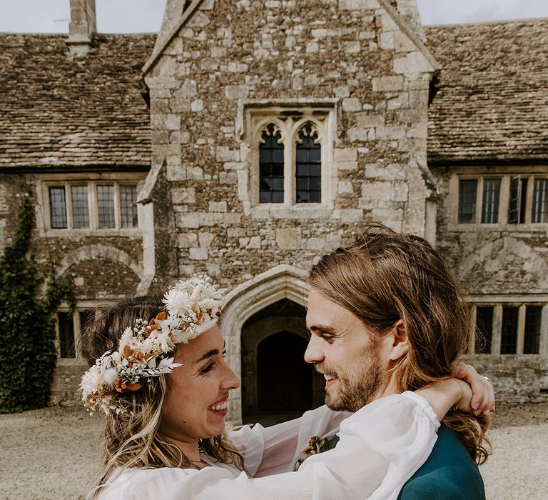 Bride wears boho styled floral crown and bell sleeved wedding dress whilst embracing her groom outdoors