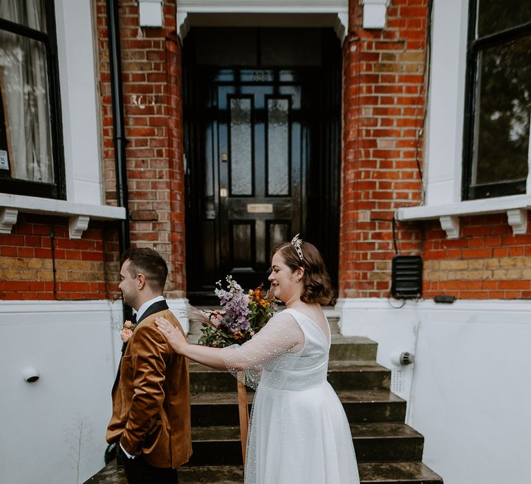 Bride and Groom do a first look outside of their home. Groom wears a burnt orange velvet blazer and Bride wears celestial themed crown and wedding dress