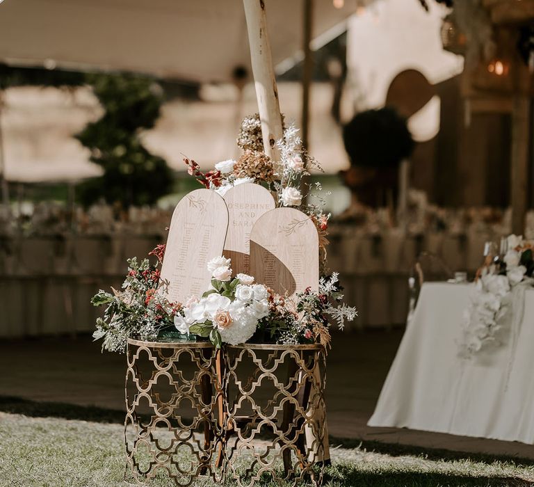 Small wooden arch seating chart with a neutral flower arrangement for marquee wedding 