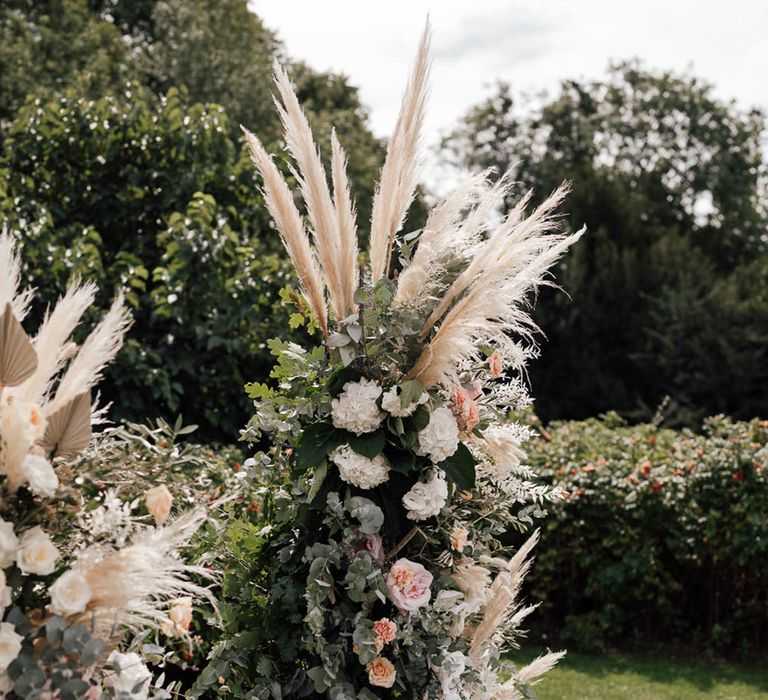 Pink and white wedding flower columns with pampas grass decorate the altar 