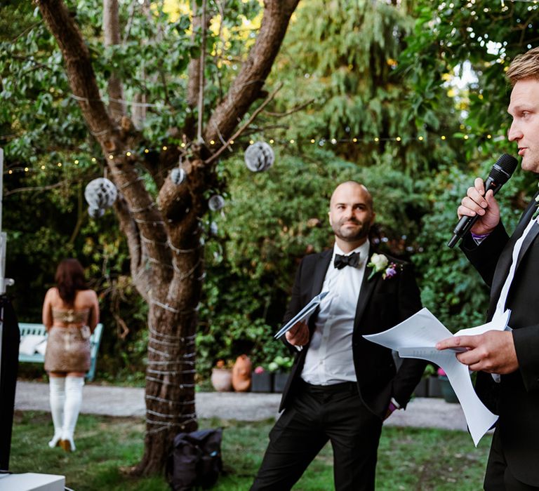 Groom in black tie gives wedding speech at family home reception with clear stretch tent 