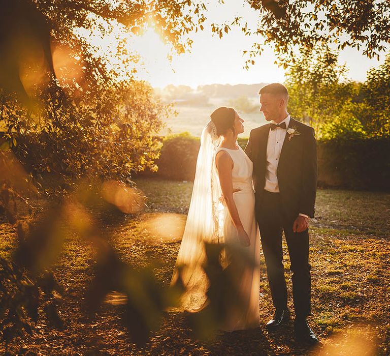 Golden hour wedding photography featuring Bride and Groom looking at each other and surrounded by greenery