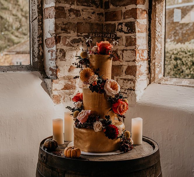 Three tier rustic wedding cake with orange and pale pink roses and dahlias decorating it with personalised wooden banner cake topper 