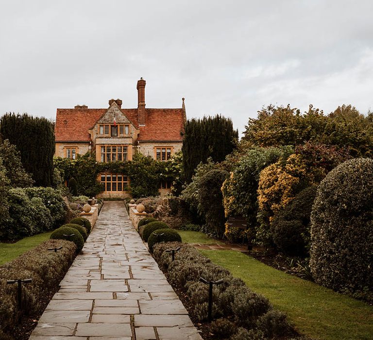 The exterior and gardens of Le Manoir Aux Quat Saisons with paving stone path leading to the venue 