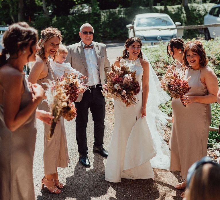 Bridesmaids in satin champagne gold halter neck bridesmaid dresses smiling with the bride in a classic white gown and the father of the bride