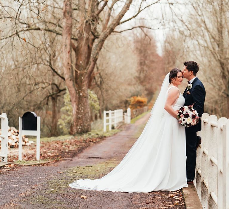 Groom in a navy suit with a leopard print pocket sqaure and white buttonhole with the bride in a classic dress with a puddle train