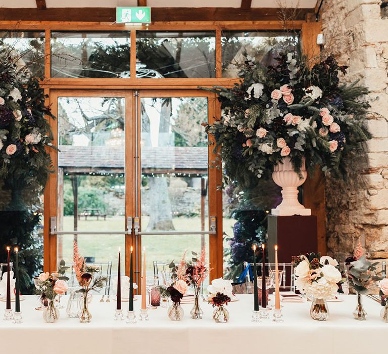 Green, burgundy, and cream taper candles with small bud vases full of blush pink and burgundy flowers 