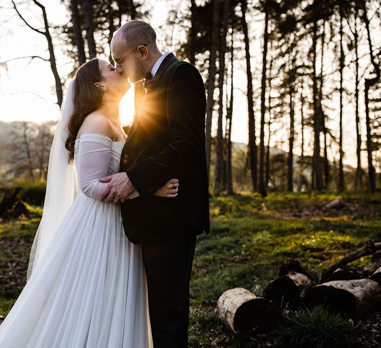 Golden hour sunset wedding couple portrait of the bride in an off the shoulder long sleeve wedding dress with the groom in a velvet tux 