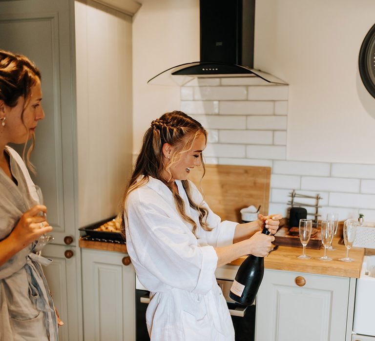 The bride pops open some alcohol in a white bridal robe as she gets ready with the bridal party for the wedding 