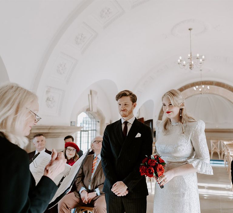 Groom in black tie with the bride in a silver wedding dress with shoulder pads standing in Normanton Church 