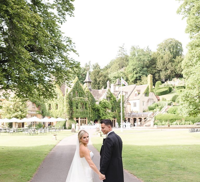 Bride in princess mermaid wedding dress with long cathedral length veil walking with the groom in a morning suit 