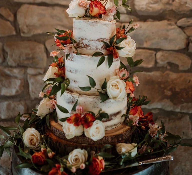 Three tiered buttercream wedding cake with gold laser cut wedding cake topper and rose and foliage wedding cake decorations on wooden cake stand 