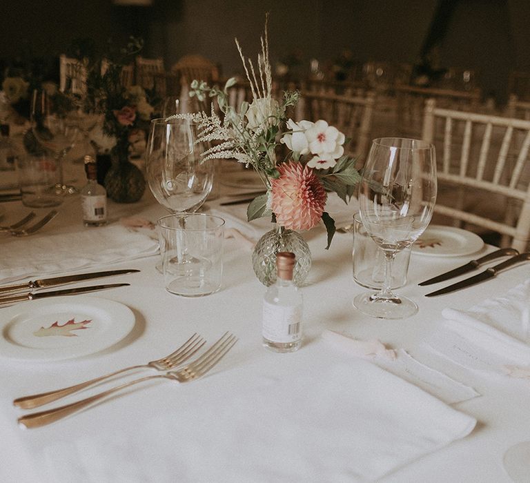 Small bud vases with pink and white wedding flowers with dahlias on a white tablecloth with white plates and napkins 