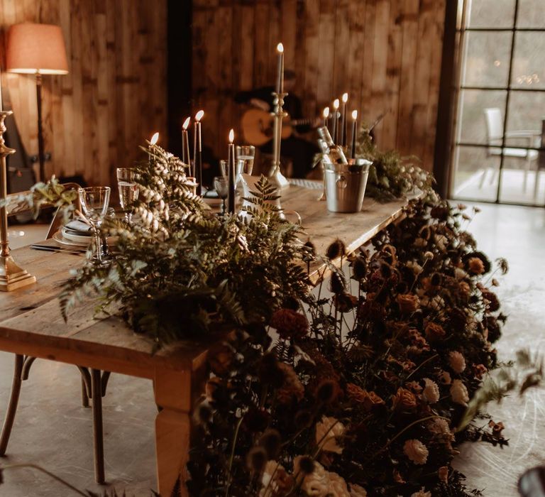 Dried sunflower, rose, peony and foliage wedding arrangements on wooden table with tapered candles and gold candlesticks on rustic wedding tablescape at Hidden River Cabins