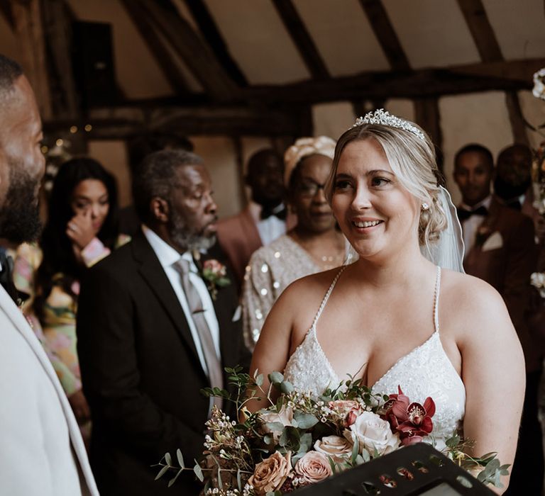 Bride wearing pearl tiara in beaded wedding dress smiling at the groom at their non-denominational ceremony 