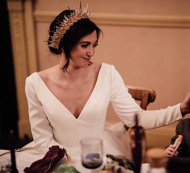 Bride in traditional wedding dress with long sleeves wearing gold bride crown sitting next to her son in brown suit 