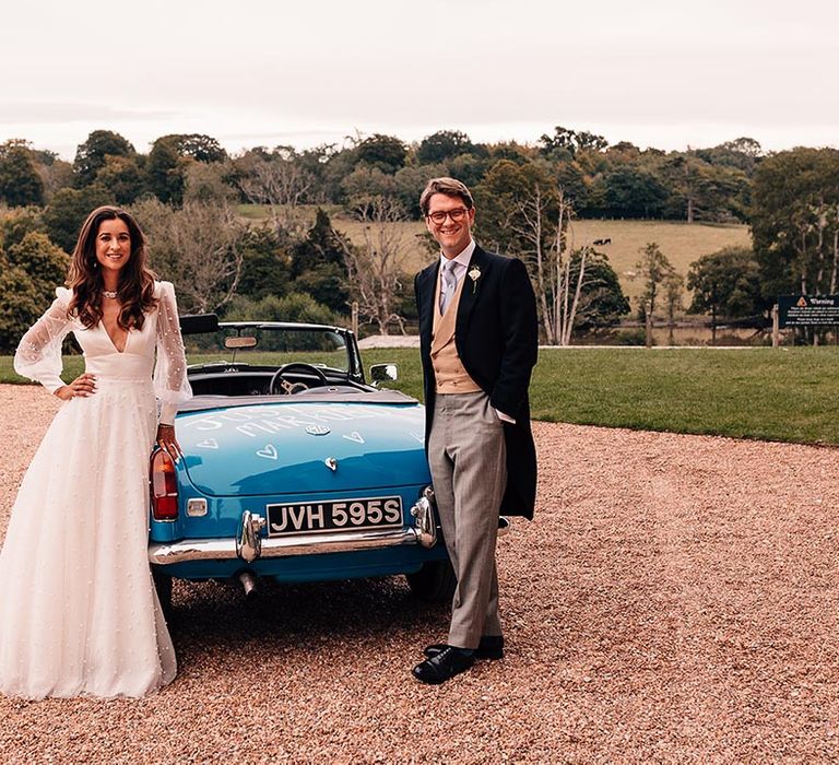 Bride and groom pose next to their MGB Roadster wedding car 