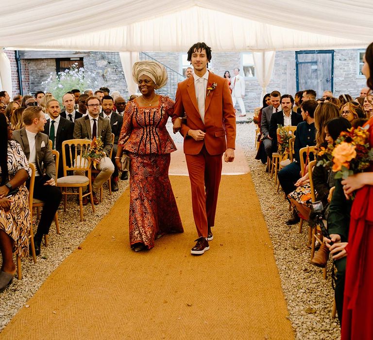 Wedding guests in orange and yellow wedding theme clothes walking down the aisle on orange wedding carpet at Broadfield Court