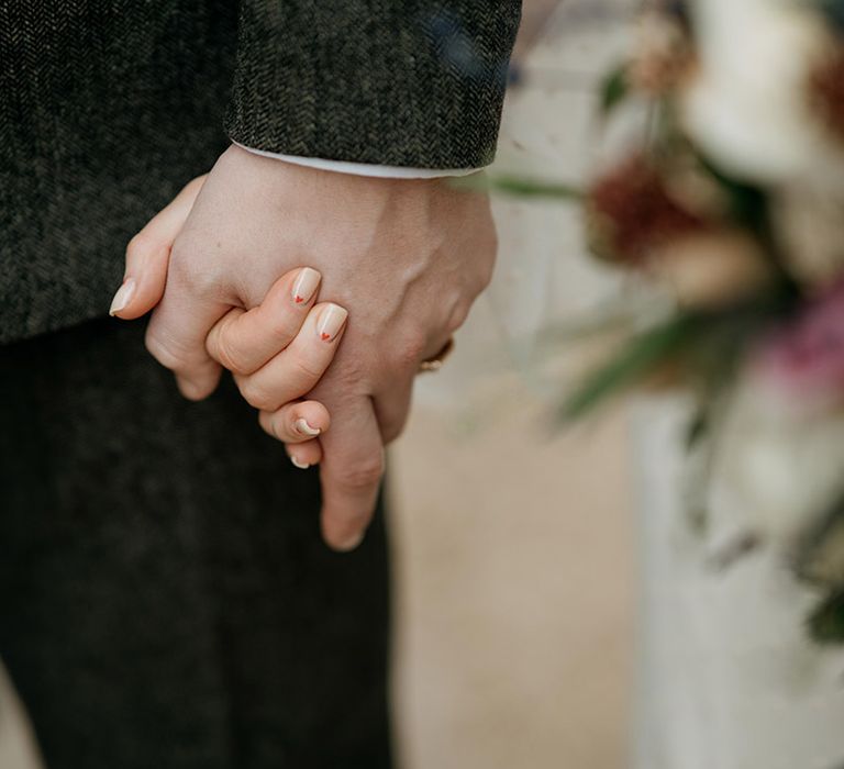 Bride holding hands with the groom with neutral wedding nails with red heart bridal nail art design 