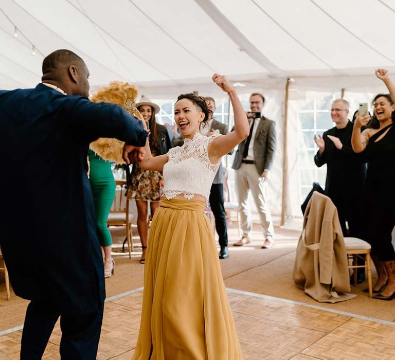 Groom in navy wedding suit dancing with bride in white mesh lace bridal crop top and yellow wedding skirt at Broadfield Court