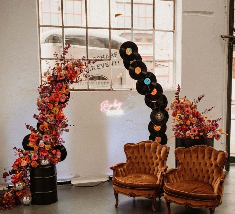 Vinyl wedding arch next to vibrant pink red and orange wedding floral arch and two crushed velvet burnt orange armchairs at German wedding