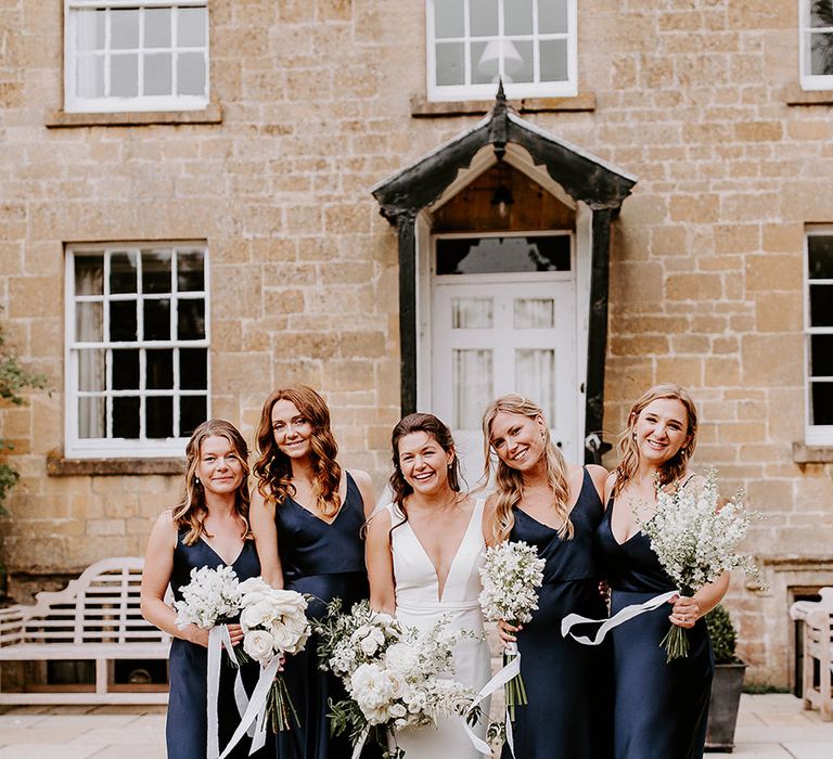 Bride in plunging Made With Love fitted wedding dress with bridesmaids in navy dresses holding white bouquets 