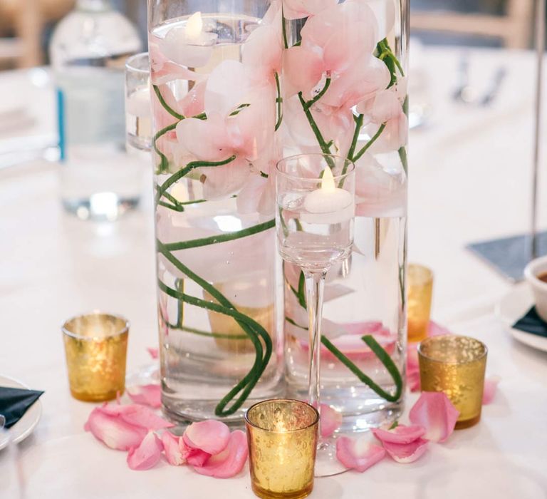 Floating flowers in hurricane vase centrepieces with small tea light candles in orange tea light candle holders