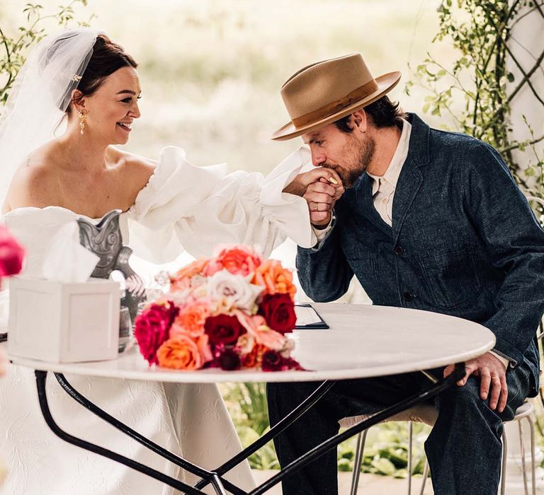 The bride in a puff sleeve gown signs the wedding register with the groom in a double denim suit and hat 