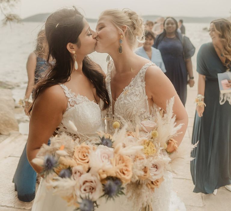 brides in lace wedding dresses holding dried and fresh flower bouquets kissing at their Croatia wedding 