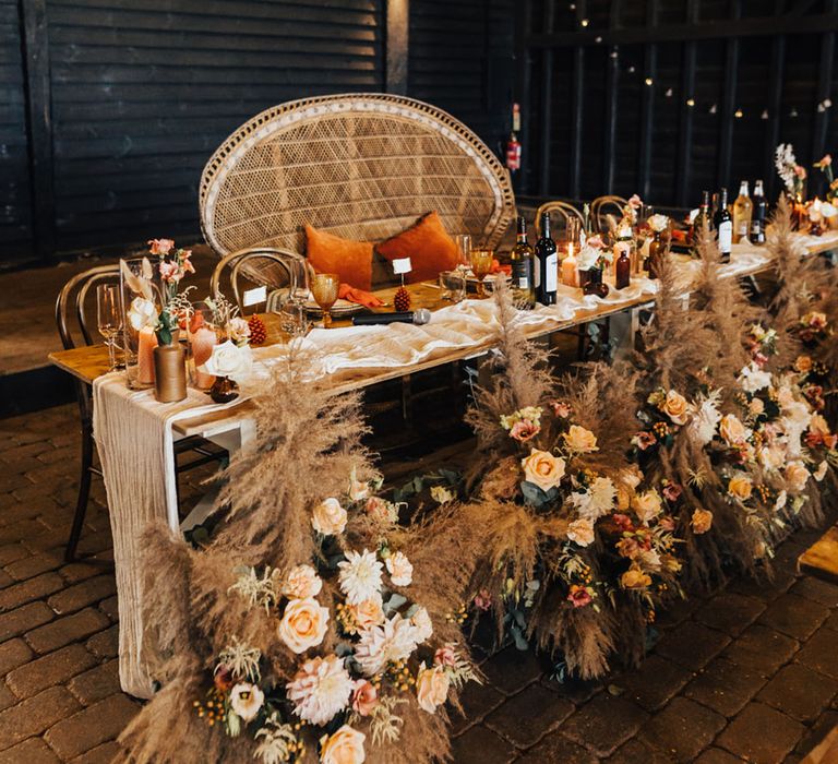 Pampas grass and orange roses decorating sweetheart table with peacock style boho chair 