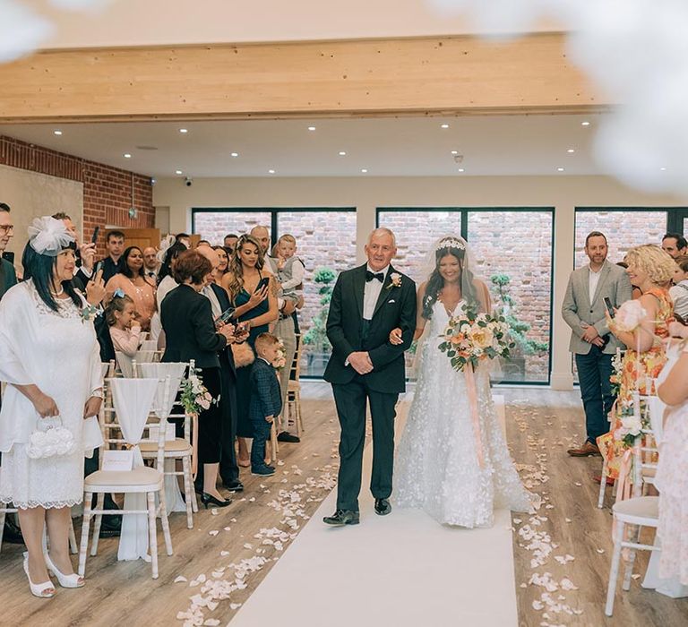 Father of the bride in a black tuxedo walks the bride down the aisle at country house wedding 