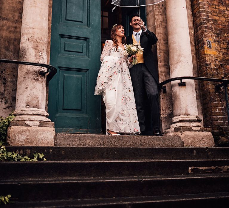 The bride and groom hold a clear umbrella on their rainy wedding day 