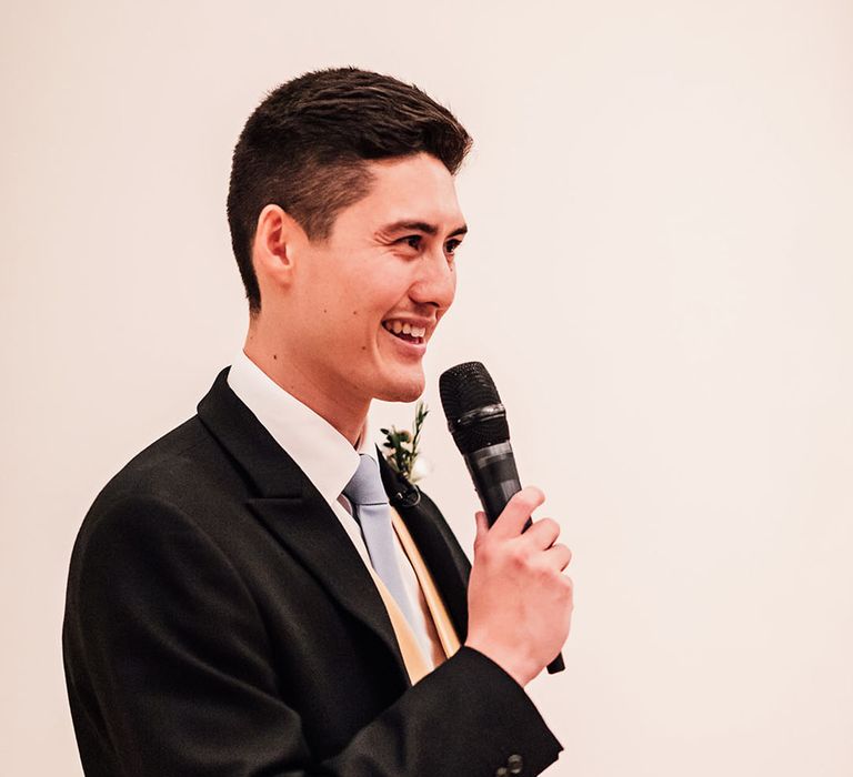 Groom in morning suit with yellow waistcoat and blue tie performs wedding speech