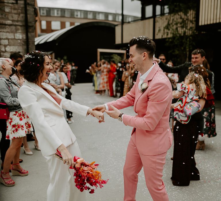 Bride and groom wearing white and pink wedding suits celebrating their wedding 