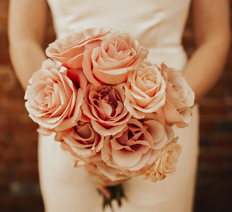 Small round pink rose bouquet held by bride with spring wedding flowers