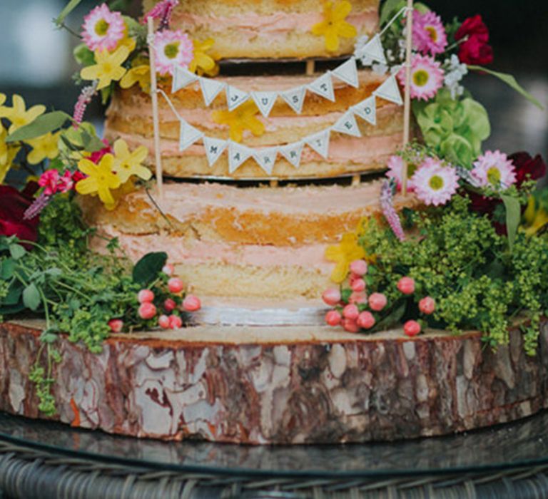 Naked wedding cake with pink icing decorated with pink and yellow flowers 