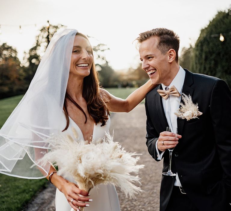 Bride wearing wedding veil with trim holding dried flower white wedding bouquet with the groom in their country house wedding 