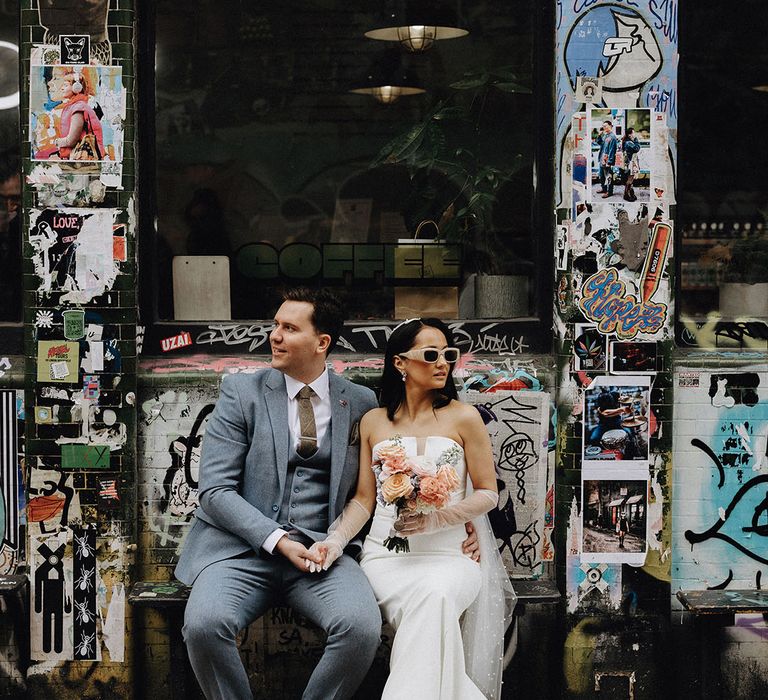 Urban city wedding with the bride wearing a pearl veil and sunglasses with the groom in a light blue wedding suit 