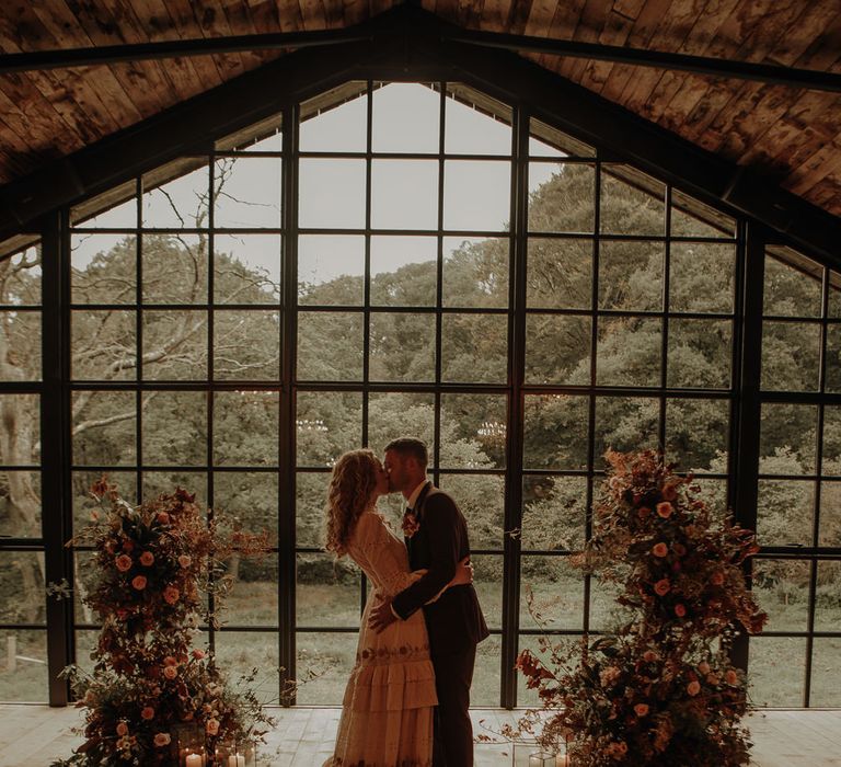 Bride and groom kissing at the altar with autumn wedding flowers 