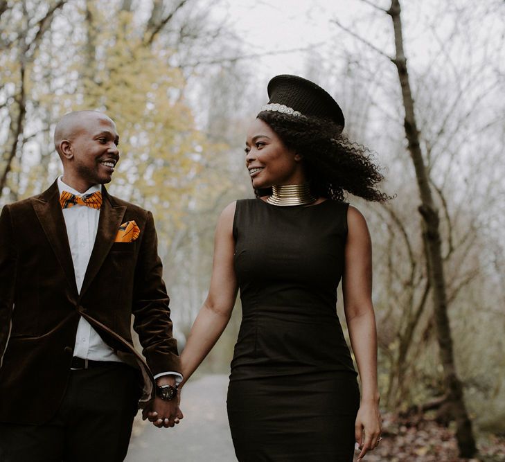 Groom in brown velvet blazer and orange bow tie and bride in black fitted dress with African print fishtail detail 