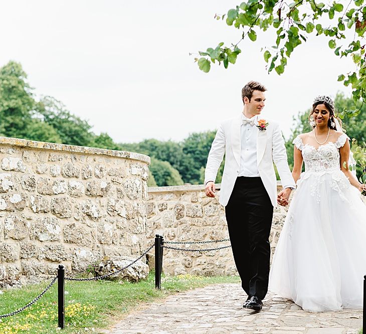 Bride in a princess Galia Lahav wedding dress with tulle skirt and appliqué design holding hands with her groom in a white tuxedo 