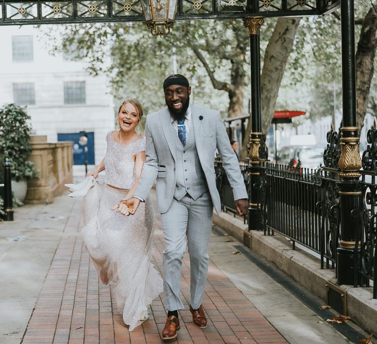 Groom in a light grey suit and brown tan brogues running outside The Landmark London with his bride in sparkly bridal separates 