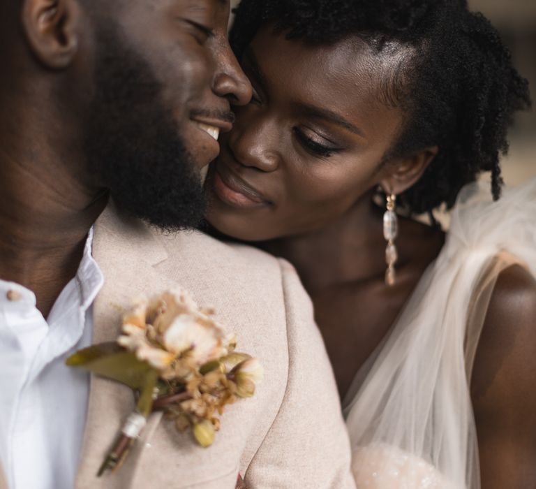 A BLack bride and groom embrace. She rests her chin on his shoulder and wears her natural hair short and loose