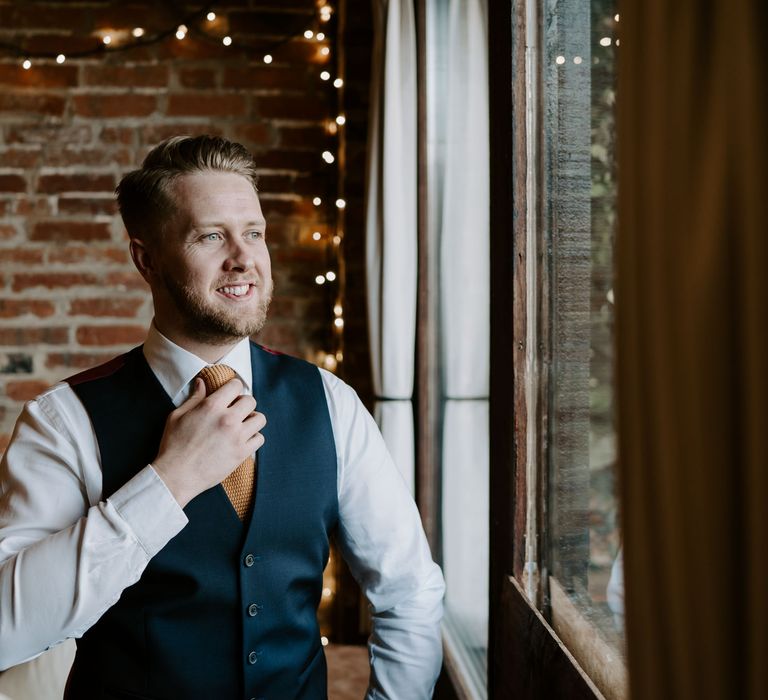 Blonde bearded groom in a navy suit and waistcoat with an orange waffle tie 