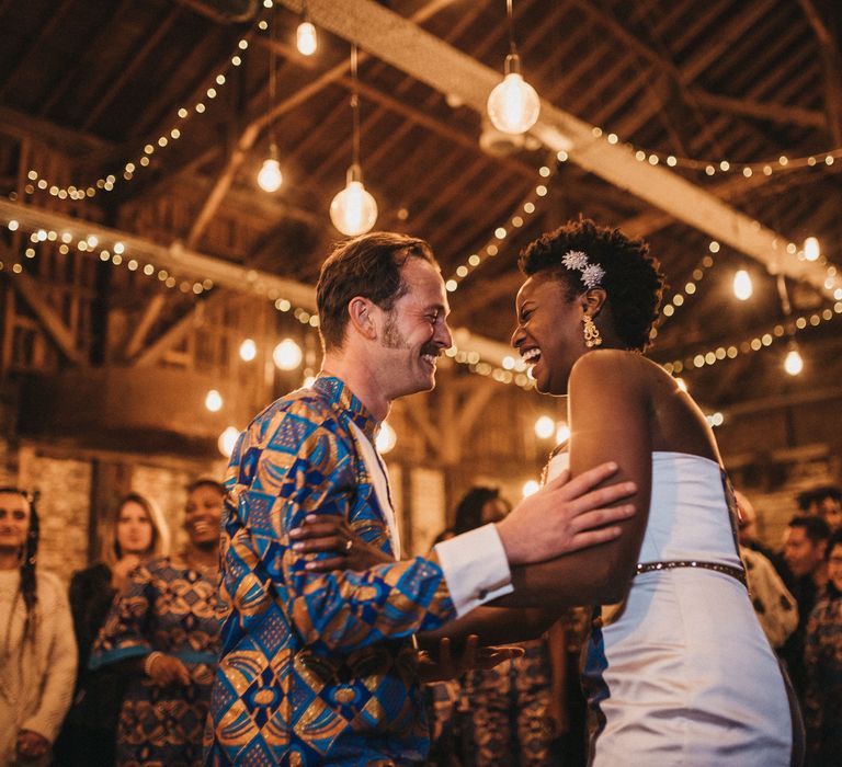 Bride and groom first dance in West African outfits under a canopy of festoon and fairy lights 