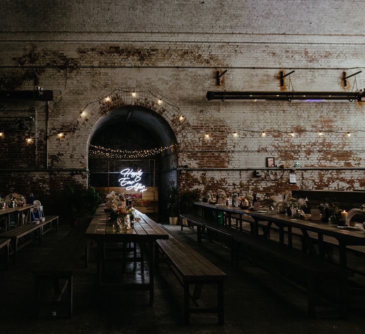 Industrial venue shot of trestle tables and 'happily ever after' neon signage against exposed brick wall