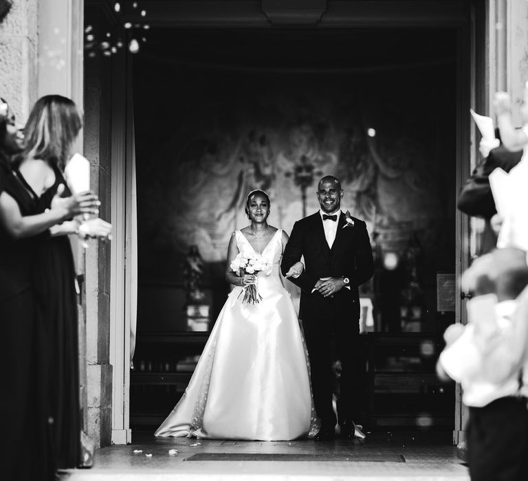 The bride and groom exit the church arm in arm, smiling as their guests wait to greet them