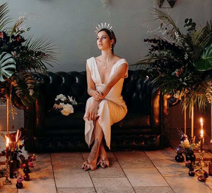 Stylish bride in a fitted wedding dress sitting on a couch with pink bow front shoes and bridal crown 