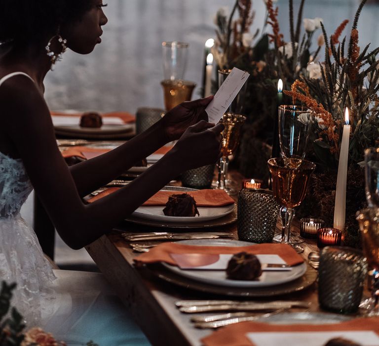 Bride sitting at an intimate candlelit table at Ponden Mill reading the wedding menu 