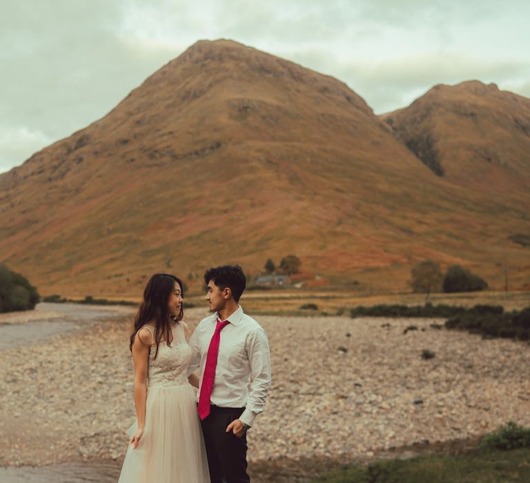 Couple stand in the Scottish countryside with mountain in the background